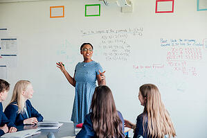 Teachers standing in the front of a class teaching in front of a white board